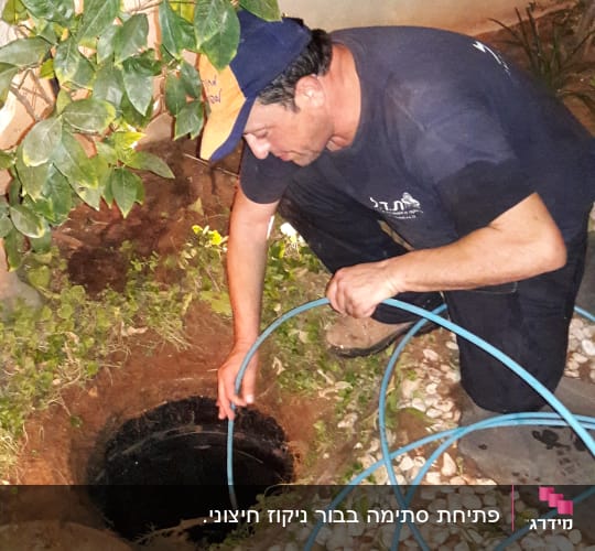 אדם מכניס צינור לתוך בור פתוח בגינה